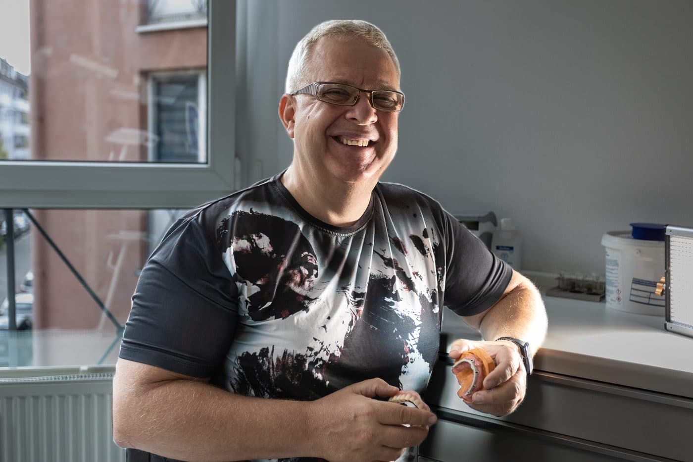 Gary Treskunov lacht in die Kamera, in den Händen zwei zahntechnische Modelle